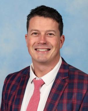 A close-up portrait of Somerville Rise principal Matt Jackson, who is wearing a check suit, pink tie and has a nose ring