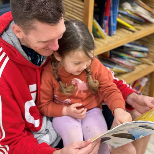 A father reads a story to his daughter sitting on his lap. 