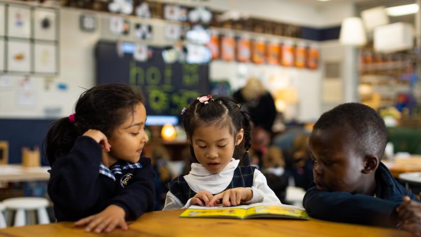 Two female students and one male student from different cultural backgrounds reading together in a classroom.