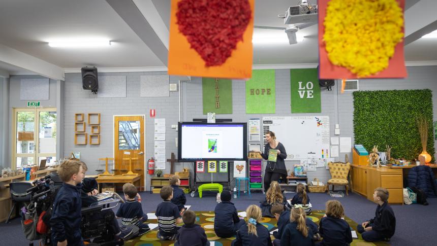 Teacher standing at the front of class, students sitting on the floor