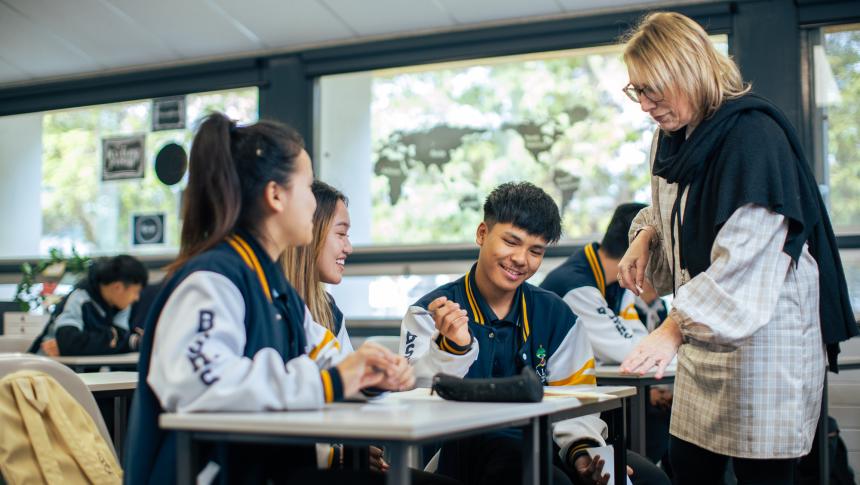 Teacher standing talking to three students sitting at a desk