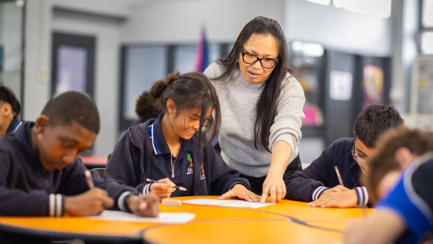 Secondary school teacher leaning over group table, giving students feedback.