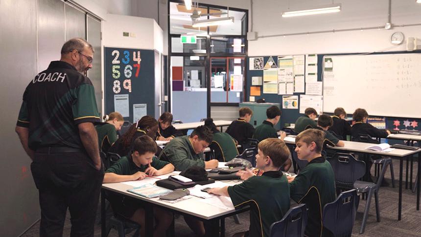 Teacher circulating classroom talking to students working at their desks