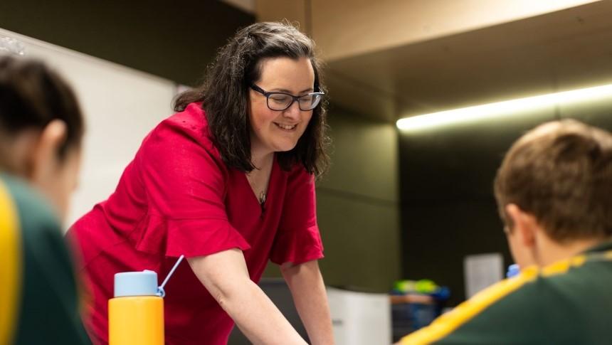 A female teacher offers support to two primary school students working at their desk