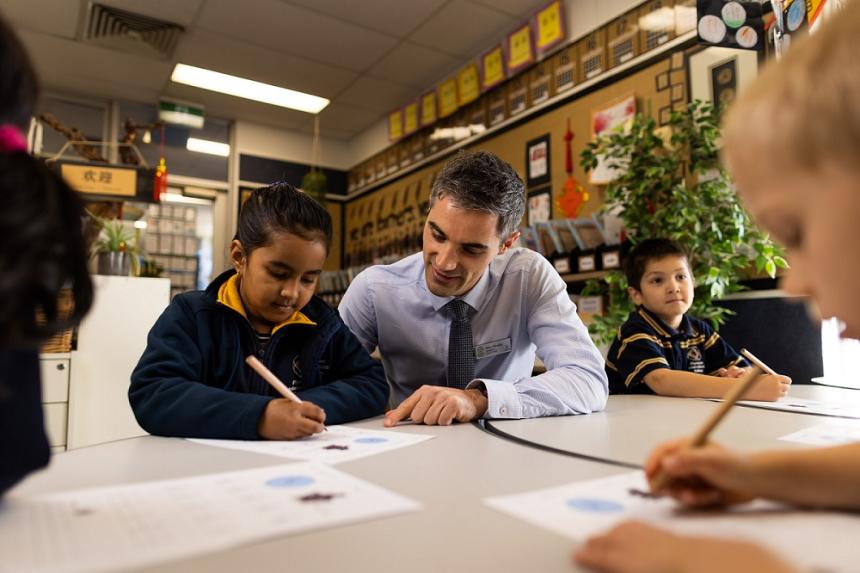 A young girl and a male teacher sitting at a desk and looking over and discussing her work. 
