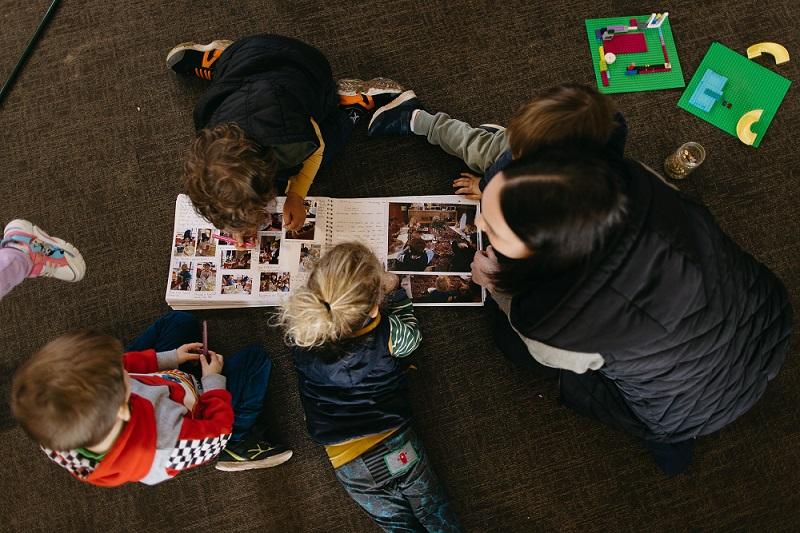 A view from above of children in a early learning setting on the floor looking at a handwritten book with images. 