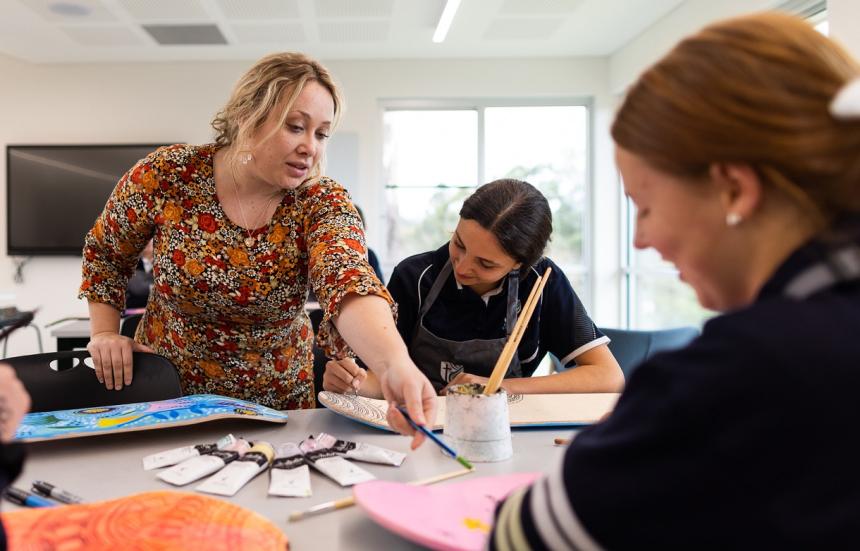 A teacher and 2 students in a secondary setting. The teacher is providing instruction and pointing at a students work. 