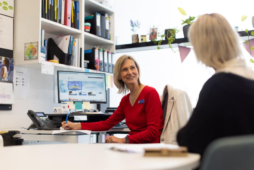 Two female teachers talking at desk in teacher's office.