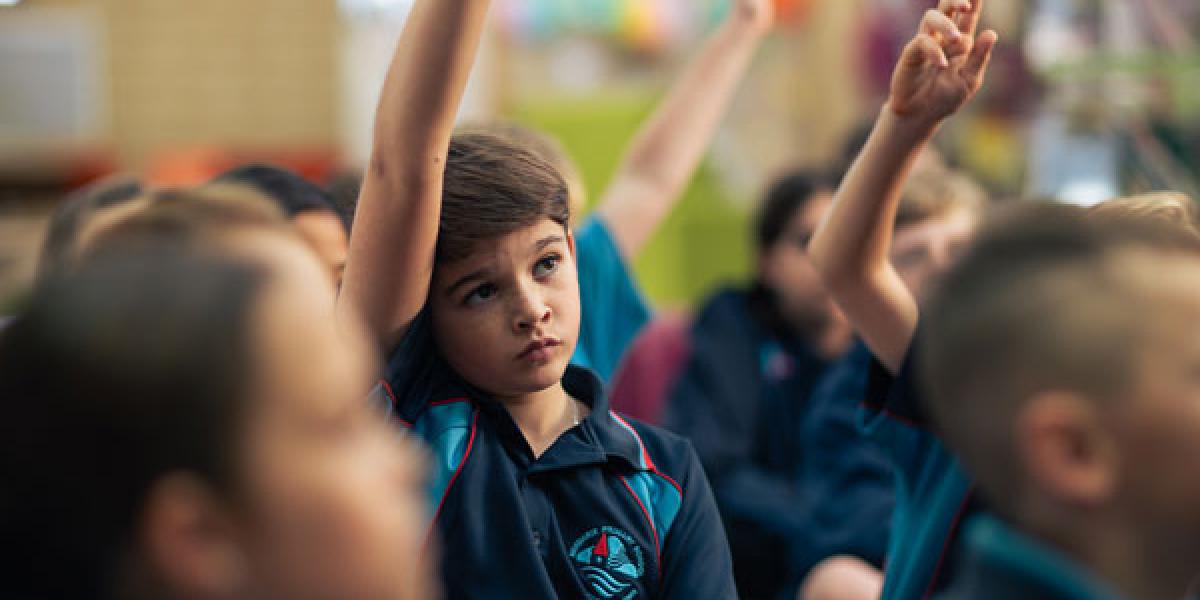 A group of children in a classroom with their hands up